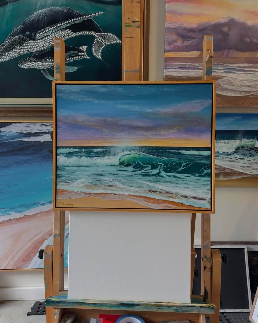 A colourful canvas of an ocean on an easel, surrounded by other ocean paintings.